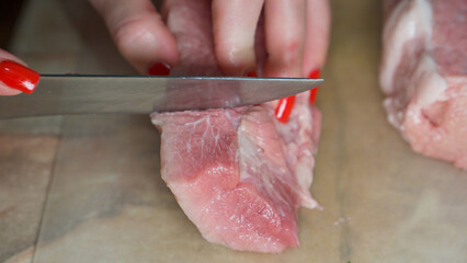Woman cuts piece of raw pork meat with kitchen knife.