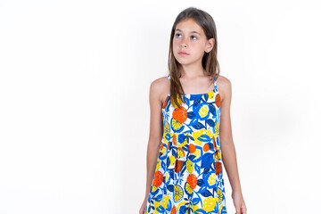 Beautiful little kid girl wearing colorful dress looking aside into empty space thoughtful
