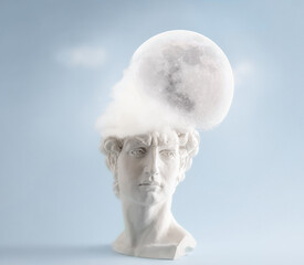 White plaster statue head of David with cloud and full moon on pastel blue background. Minimal art poster.