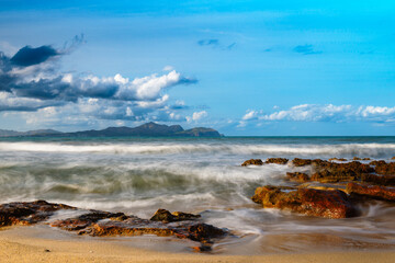 Fototapeta na wymiar High waves hitting the shore and splashing over the rocks on a beautiful cloudy day.