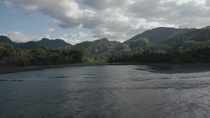 Drone footage over the lakeshore with green dense woods and mountains in the background