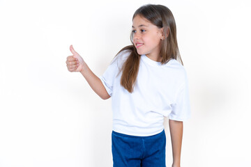 Beautiful little kid girl wearing white T-shirt Looking proud, smiling doing thumbs up gesture to the side. Good job!