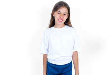 Beautiful kid girl wearing white T-shirt keeps teeth clenched, frowns face in dissatisfaction,...