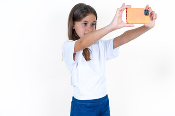 Beautiful kid girl wearing white T-shirt taking a selfie to post it on social media or having a...