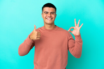 Young handsome man over isolated blue background showing ok sign and thumb up gesture