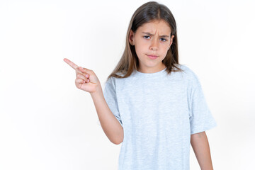 Serious Beautiful little kid girl wearing blue T-shirt smirks face points away on copy space shows...