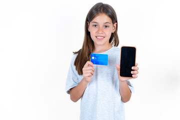 Fototapeta premium Photo of adorable Beautiful little kid girl wearing blue T-shirt holding credit card and Smartphone. Reserved for online purchases