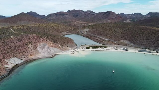 Aerial dolly shot of Playa Pichilingue near the ferry and cruise port of La Paz, Baja California Sur, Mexico with sandy beach, idyllic coastline and majestic mountains in the background