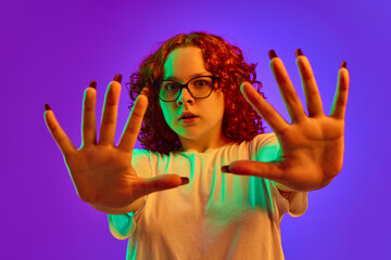 Teen girl emotional spreading hands with terrified face against purple background in neon light. Concept of human emotions, lifestyle, youth, facial expression. Ad