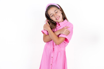 Beautiful little kid girl wearing pink dress Hugging oneself happy and positive, smiling confident. Self love and self care