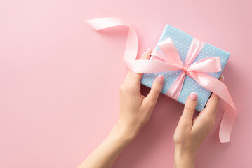 First person top view glimpse of woman's hands interacting with pastel blue gift box featuring...