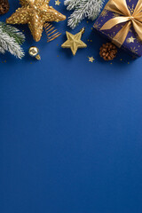 Luminous Blue and Gold Gift Inspiration. Top view vertical shot of dazzling present, ornaments, sparkling stars decor, confetti, pinecone, frosty fir twigs on rich blue backdrop with room for your ad