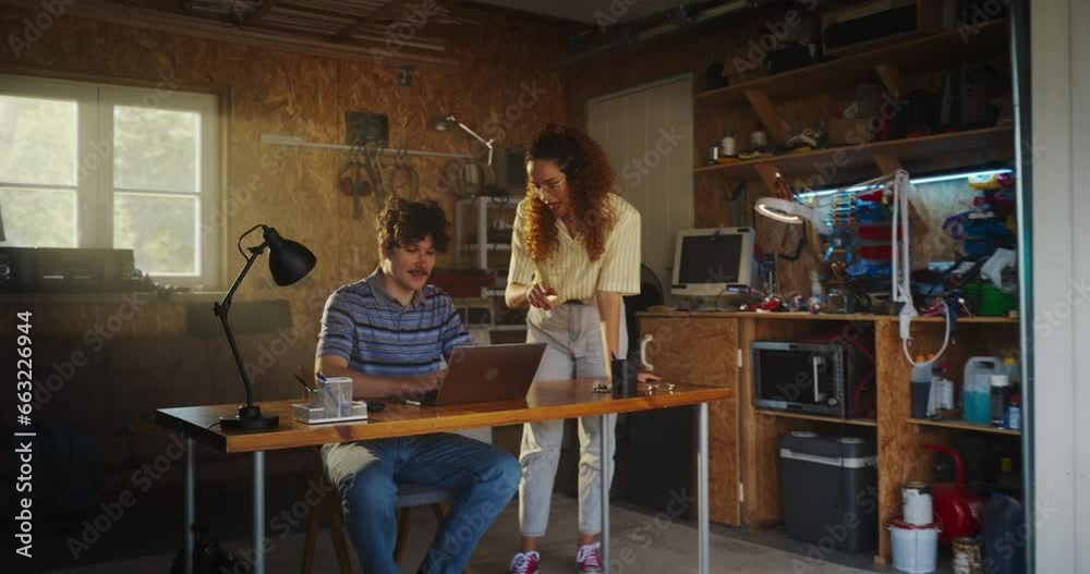 Fototapete Caucasian Male Software Engineer And Hispanic Female User Interface Designer Talking And Using Laptop Computer in Garage At Home. Diverse Young Startup Founders Working On Innovative Online Service.