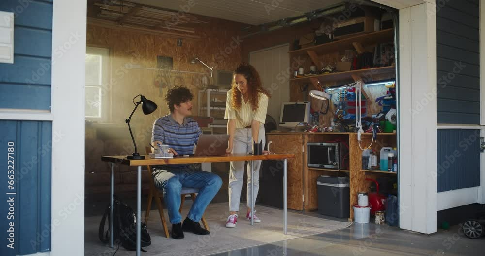 Fototapete Caucasian Male Software Developer And Hispanic Female User Interface Designer Talking And Using Laptop Computer in Garage At Home. Diverse Young Startup Founders Working On Innovative Online Service.