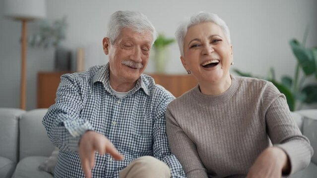 Smiling happy senior couple man and woman calling video chat and emotionally talking looking at camera. They wave hands greeting talker. Modern technologies in everyday life of old people concept.