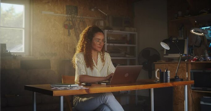 Hispanic Female Programmer Writing Code On Laptop Computer In Garage At Home. Woman Working On Innovative Software As A Service Startup For Business. Digital Entrepreneur Starting Company Concept.