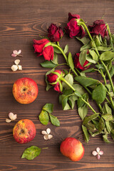 Withered, decaying, roses flowers and apples on brown wooden background. top view, close up.