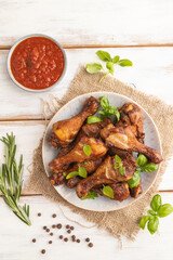 Smoked chicken legs on a ceramic plate on a white wooden background. Top view, close up.