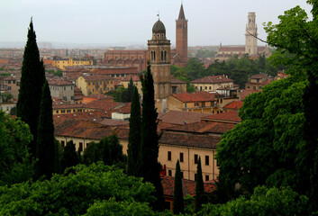 Obraz premium Photo of a view of the historic part of Verona, Italy, with the cathedral and bell tower and cypress trees in the foreground in a light fog during the rain