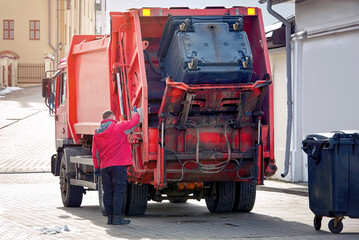 Refuse collector man unload dustbin in rear load garbage truck. Trash removal work in the city...