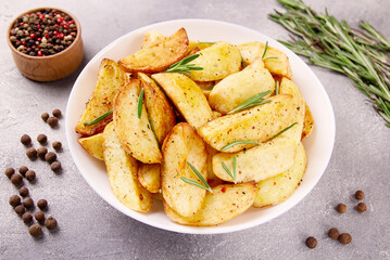 Baked potato wedges with seasonings on a plate on a gray stone.