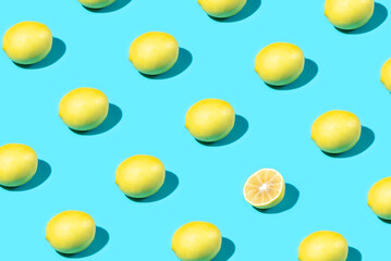 Trendy Summer food pattern made with yellow lemon and one slice on bright light blue background. Minimal summer concept.