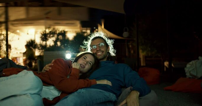 Close-up shot: a couple in love are lying on beanbag chairs and watching a movie. A party outside the city. Rest in the country house