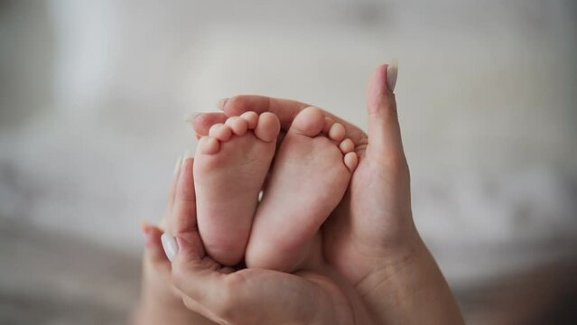 Mom gently tickling baby's tiny feet one finger, hands close-up. Congenital reflex finger flexion in infants, healthy body reaction. Mother enjoying motherhood checks baby health. Feet heart shape.