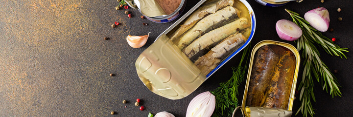 Different open tin cans with canned fish among spices and herbs banner, canned salmon and mackerel,...