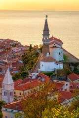 Piran Old Town, Slovenia, scenic cityscape. Top view of medieval architecture with church of St. George, Adriatic Sea and sky in sunset light from Old City Walls, outdoor travel background - 663241524