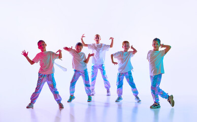 Naklejka premium Cute talented children dressed in fashion clothes with bright glittered makeup performing new dance in neon light over white studio background.