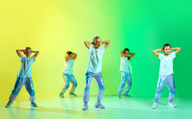 Cute talented children dressed in style clothes with bright glittered makeup performing new dance tricks synchronous movements over gradient background.