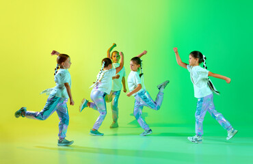 Cute children wearing fashion trendy outfit with bright glittered makeup performing new dance tricks synchronous movements over gradient background.