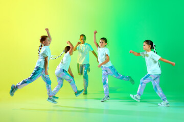 Fototapeta na wymiar Cute children wearing fashion trendy outfit with bright glittered makeup dancing synchronous in motion over gradient background in neon light.