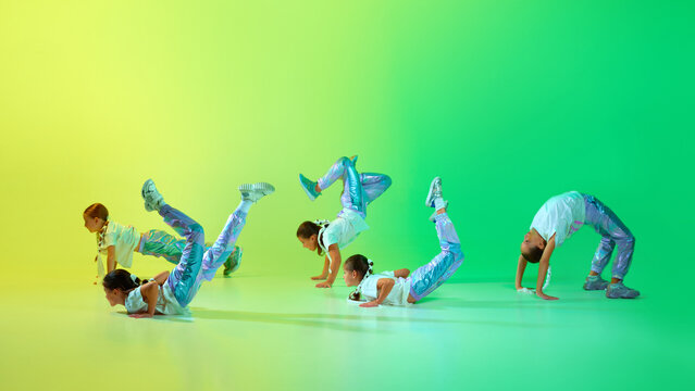 Group of girls wearing sporty trendy outfit with bright glittered makeup dancing synchronous choreography class over gradient background in neon light.