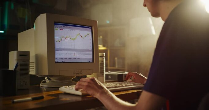 Caucasian Male Stock Trader Using Old Desktop Computer With Financial Candlestick Chart In Retro Garage. Man Analyzing Price Action Before Entering Trade, Starting Investment Fund In Nineties.