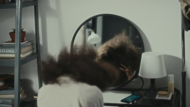 Black teenage girl sitting at home, looking at reflection in mirror, feeling nervous and hating herself n