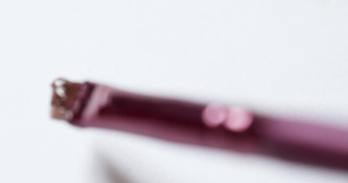 Smudging some peach pink lip-moisturizing balm, with a brush applicator on a white sheet of paper.