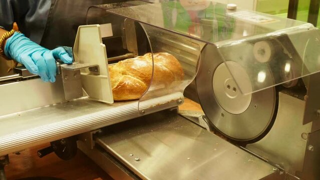 A baker slicing a loaf of sourdough bread using a machine inside a local bakery in Bangkok, Thailand.