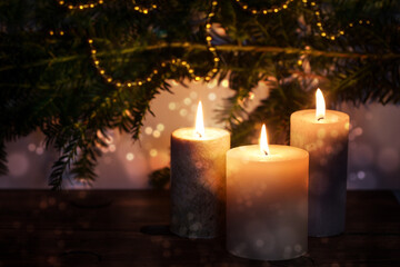 Three burning candles in front of dark fir branches with Christmas decoration and bokeh bubbles,...