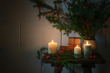 Christmas time with burning candles, gifts, evergreen branches and decoration on a small wooden table, cozy warm light in the dark season, copy space, selected focus