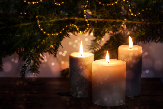 Three burning candles in front of dark fir branches with Christmas decoration and bokeh bubbles, seasonal holiday greeting card, copy space, selected focus