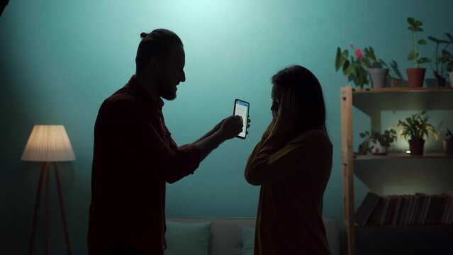 Silhouette of a husband and wife arguing near a wall, a man accusing his girlfriend of adultery, showing a smartphone screen with messages from her lover