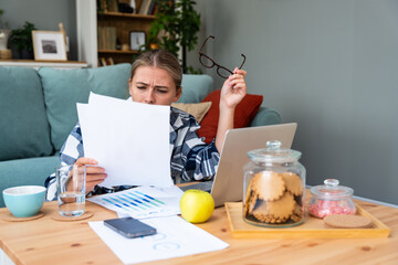 Fototapeta na wymiar Young business woman owner of small start up company, accountant looking financial statistics with worried and confused facial expression. Female adviser expert working at home office