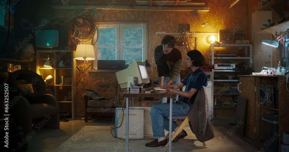 Poster two caucasian male tech startup founders using old desktop computer in retro garage in the evening. 