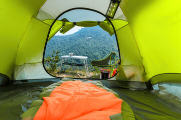 Personal perspective of a person relaxing and looking at the view from his green tent on top of the mountain. He has a table and camping chair for himself.