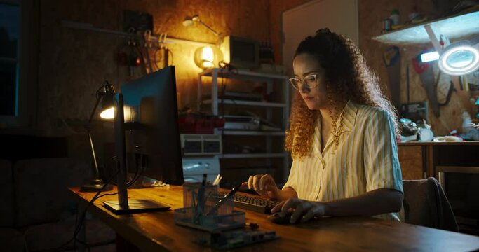 Hispanic Female Software Engineer Programming on Desktop Computer In Retro Garage Late At Night. Ambitious Woman Starting Technological Startup Company. Coding Innovative Online Service At Home.