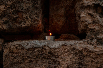A small candle burning in the dark area among the stones inside the mountain. Background concept.
