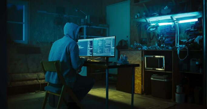 Backview Of Anonymous Professional Programmer Obsessively Writing a Code on His Desktop Computer, Late at Night In Garage. IT Specialist Ethical Hacker Working on Finding Software Vulnerabilities.