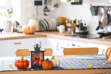 Decor of white classic kitchen with pumpkins, garlands, latern for Halloween and harvest with figurine of house. Autumn mood in home interior, modern loft style. real estate, insurance, mortgage